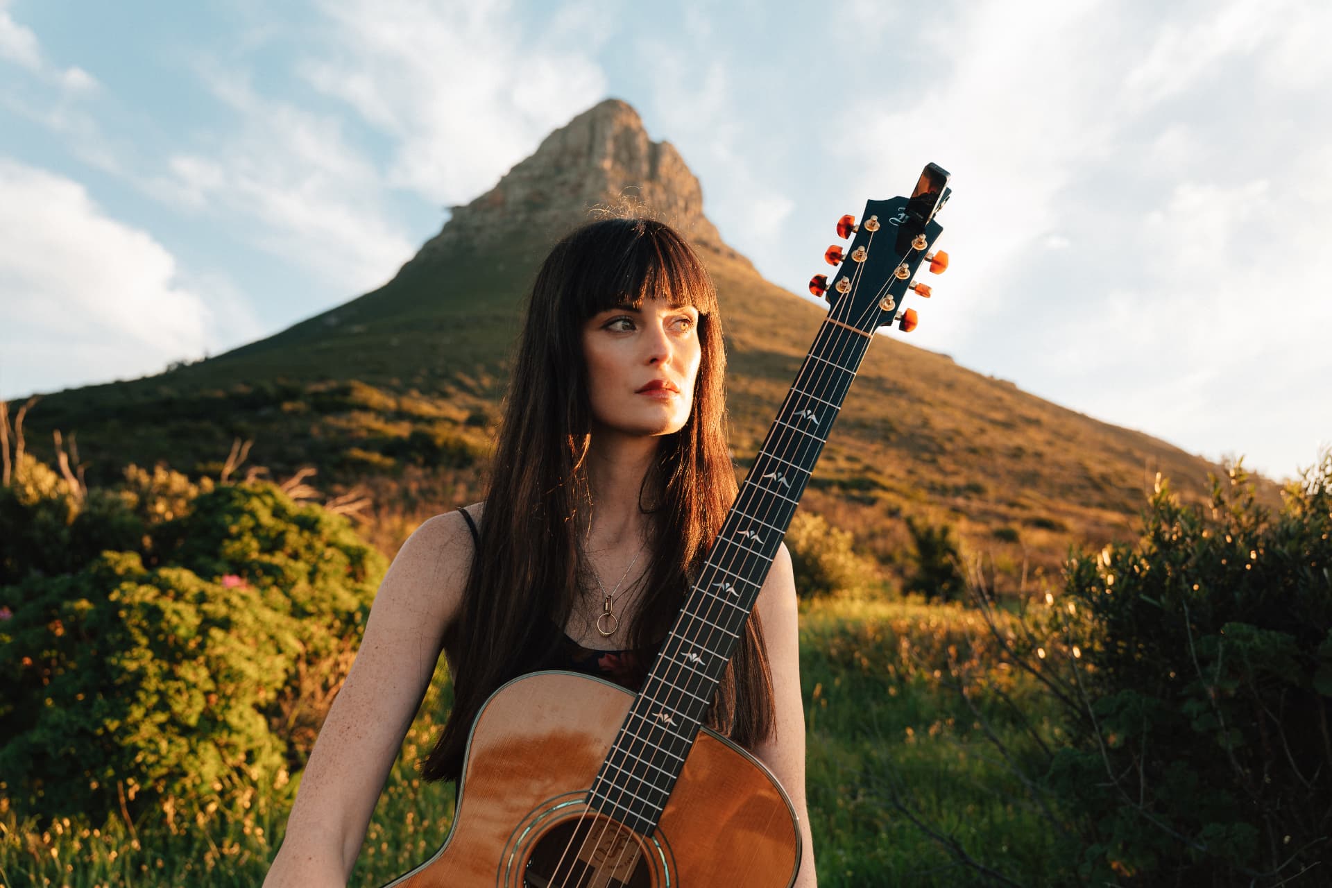 Grace de la Hunt holding her acoustic guitar in front of Lion's Head, Cape Town